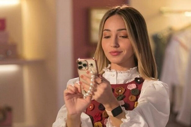 Atriz Mharessa Fernanda, de camisa mangalonga branca e sobreposição estampada com bolas coloridas, mexendo no celular, durante gravação da série Todas as Garotas em Mim (Record TV)