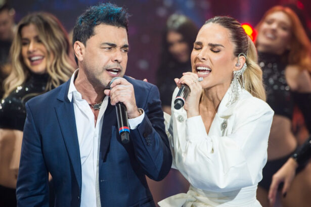 Zezé di Camargo de blazer azul e camisa social branca, com o microfone na mão esquerda ao lado de Wanessa, de camisa social branca, com microfone na mão esquerda durante gravação do Faustão na Band, da Band