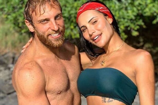 Leo Lins sorrindo, sem camisa, abraçando Aline Mineiro, que está sorrindo, de biquine verde e bandana na cabeça