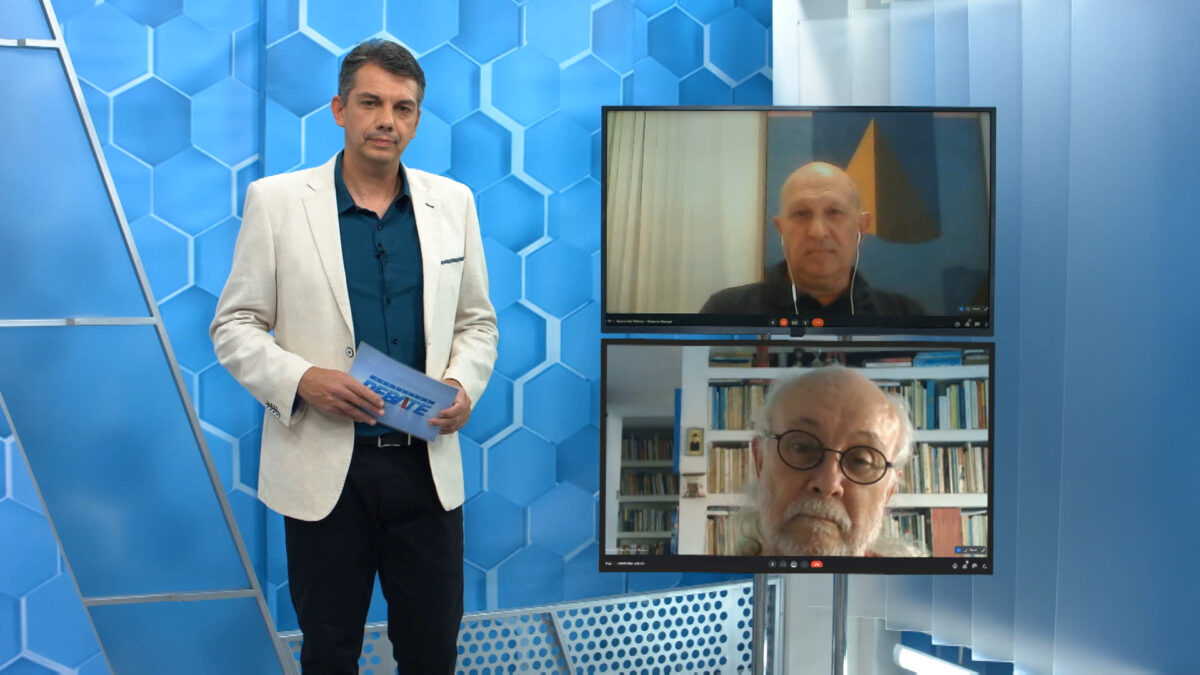Jornalista Renato Dias de blazer branco, camisa azul e calça preta segurando as fichas do programa; Roberto Bertani no visor superior, de camisa azul e crachá, sentado, com expressão séria; Antonio Albino de óculos de grau, sentado, concentrado no debate