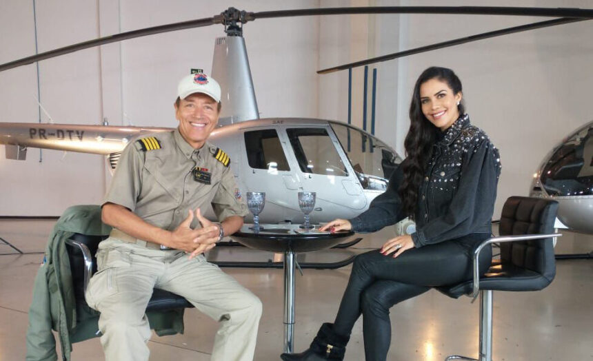 Comandante Hamilton de frente para Daniela Albuquerque, em trecho da entrevista, com um helicóptero ao fundo