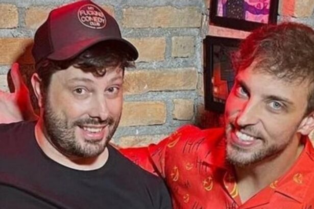 Danilo Gentili sorrindo, de camisa preta e chapéu cor de vinho; Leo Lins sorrindo, de camisa social vermelha