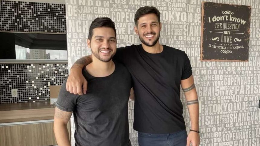 Diogo e Rodrigo Mussi abraçados, em frente uma parede de apartamento