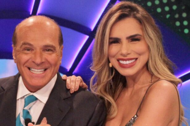 Marcelo de Carvalho de palitó preto, camisa social branca e gravata azul ao lado de Erika Schneider, sorrindo, de microfone no rosto e vestido prata durante gravação do "O Céu é o Limite", da RedeTV!