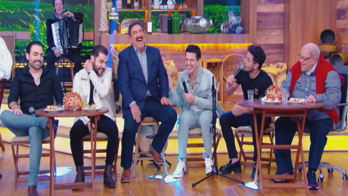 Ratinho centado num banco de palitó e camisa azul, ao lado das duplas Ratinho conversa com Hugo & Guilherme e Guilherme & Benuto durante gravação do Boteco do Ratinho, do SBT