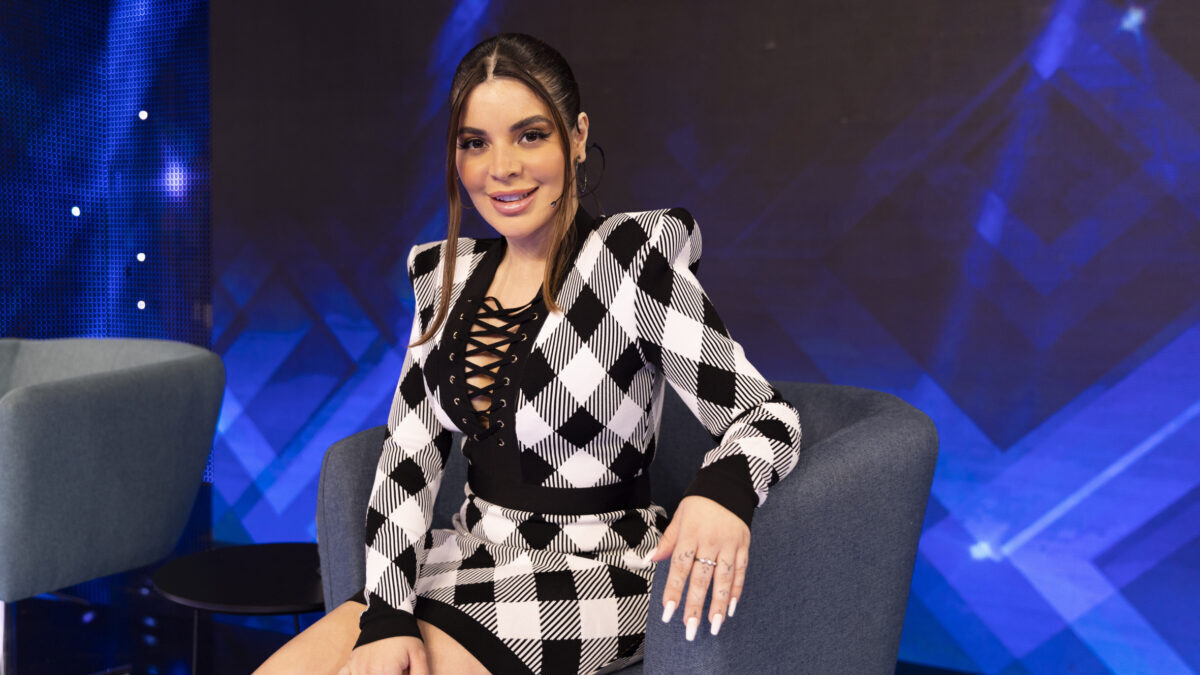 Gkay sentada em uma poltrona em um estúdio com o fundo de um telão azul