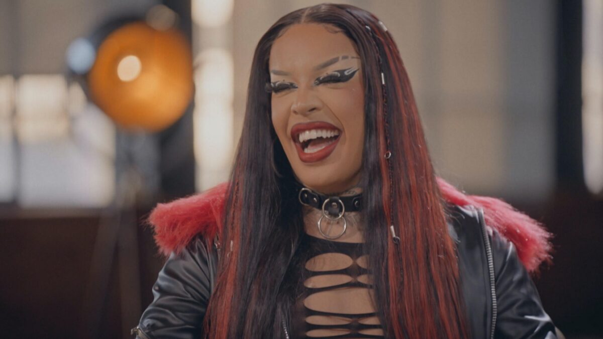 Gloria Groove sorrindo, de camisa de capuz preta durante gravação do Conversa com Bial, da TV Globo