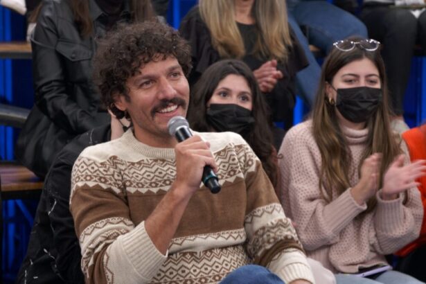 Guito, que interpreta Tibério em "Pantanal", de camisa manga longa marron, bege e branco, segurando o microfone com a mão direita e sorrindo durante entrevista do Altas Horas, da TV Globo