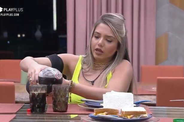 Karol sentada na mesa com uma garrafa de refrigerante nas mãos.