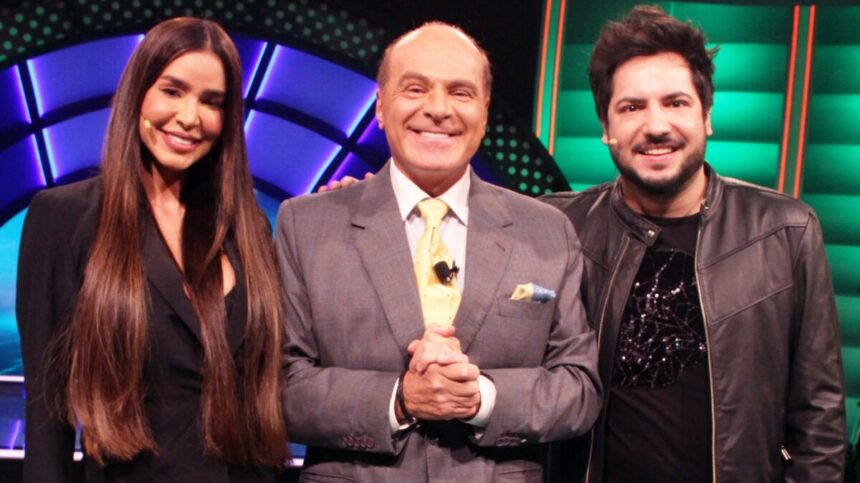 Kerline de vestido preto, cabelo solto, sorrindo; Marcelo de Carvalho sorrindo, de mãos dadas, de palitó cinza e gravata verde clara; Thiago de jaqueta de couro, camisa e calça jeans preta, sorrindo durante gravação do programa O Céu é o Limite, da RedeTV!