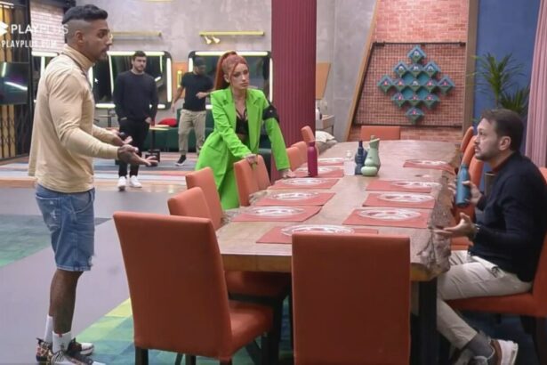 Albert sentado na mesa do Power Couple Brasil discutindo com Matheus e Brenda que estão em pé