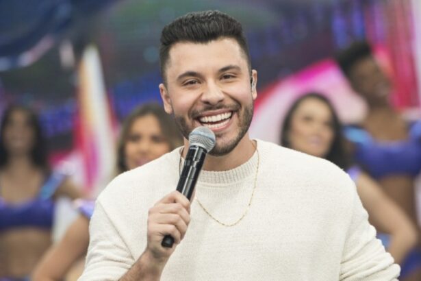 Murilo Huff com camisa manga-longa branca, sorrindo, com microfone na mão esquerda durante apresentação no Faustão na Band