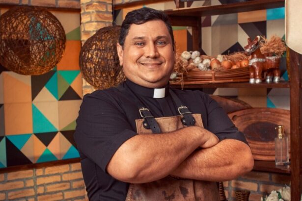 Padre Chef Evandro de camisa preta e avental marrom, sorrindo, com os braços cruzados durante gravação do Sabor de Vida, da TV Aparecida