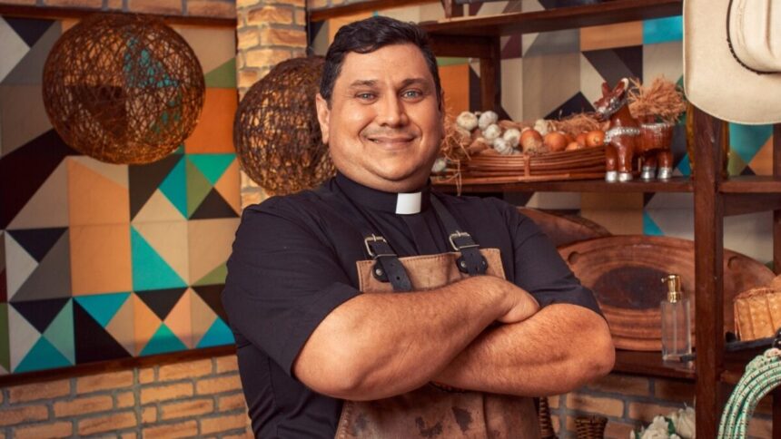 Padre Chef Evandro de camisa preta e avental marrom, sorrindo, com os braços cruzados durante gravação do Sabor de Vida, da TV Aparecida