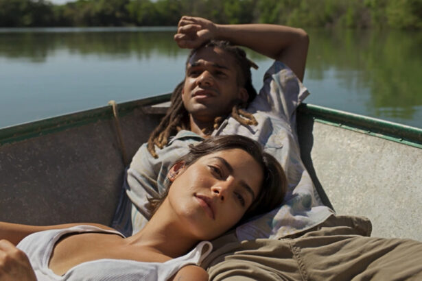 Lucas Leto (Marcelo) e Julia Dalavia (Guta) em trecho da novela Pantanal, a bordo de uma canoa no rio. Ela está deitado sobre o colo dele