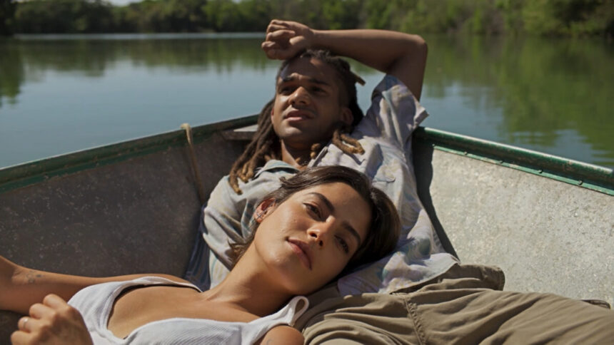 Lucas Leto (Marcelo) e Julia Dalavia (Guta) em trecho da novela Pantanal, a bordo de uma canoa no rio. Ela está deitado sobre o colo dele