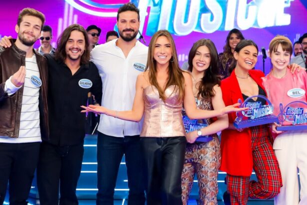 Patrícia Abravanel sorrindo, de camisa brilhosa e calça preta, com os braços abertos no meio dos dois times do Disputa Musical