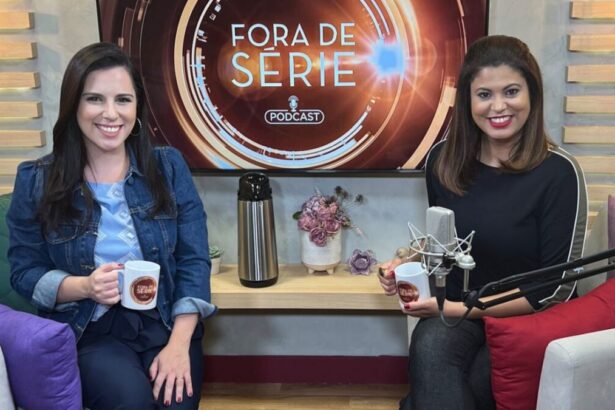 Ana Carolina Curyde camisa jeans azul escuro e regata azul claro, sorrindo, segurando uma caneca com a logo oficial do podcast fora de série; Raphaela Castro de camisa e calça preta jeans, sentada ao lado de uma almofada vermelha, ao lado da bancada