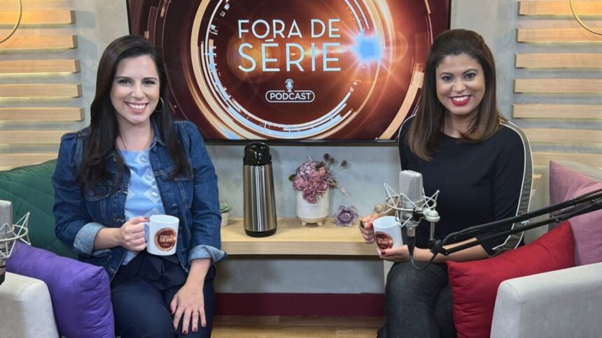 Ana Carolina Curyde camisa jeans azul escuro e regata azul claro, sorrindo, segurando uma caneca com a logo oficial do podcast fora de série; Raphaela Castro de camisa e calça preta jeans, sentada ao lado de uma almofada vermelha, ao lado da bancada