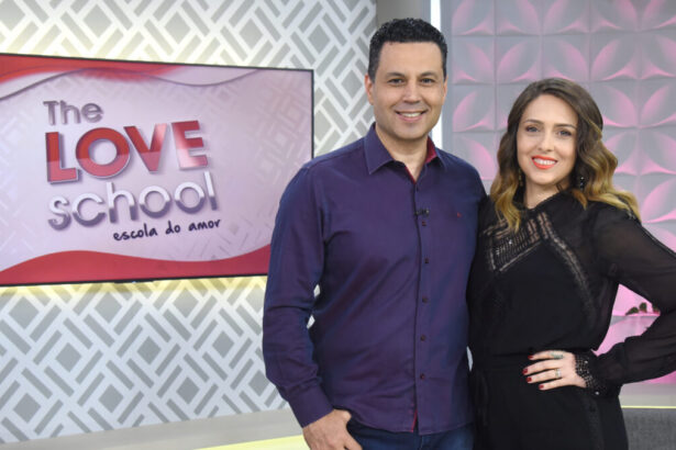 Renato e Cristiane Cardoso abraçados nos estúdios do The Love School, com a televisão ao fundo tendo o logo do programa