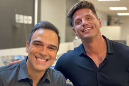 Tadeu Schmidt e Fernando Fernandes abraçados, em uma sala de reunião, nos bastidores da TV Globo