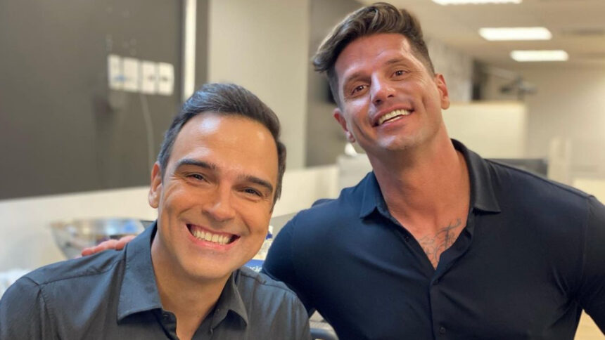 Tadeu Schmidt e Fernando Fernandes abraçados, em uma sala de reunião, nos bastidores da TV Globo