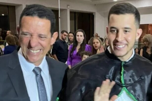 José Maria Trindade sorrindo, de palitó e gravata ao lado de e José Vitor Trindade de bata de formatura, durante colação de grau em 2020