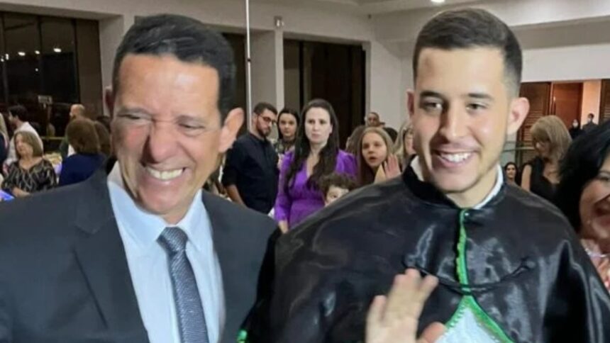 José Maria Trindade sorrindo, de palitó e gravata ao lado de e José Vitor Trindade de bata de formatura, durante colação de grau em 2020