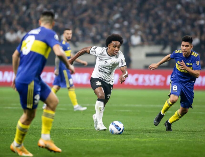 Willian em campo com a camisa do Corinthians, tendo jogadores do Boca Juniors ao seu redor