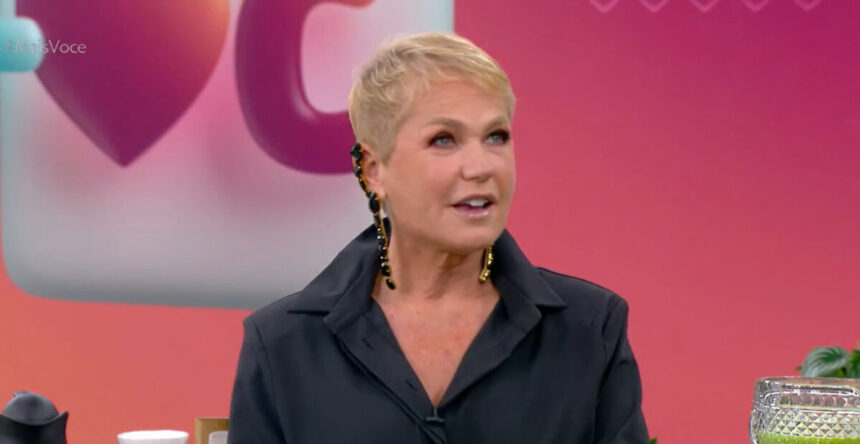 Xuxa Meneghel nos estúdios do Mais Você, com o telão ao fundo, tendo o logo do programa projetado