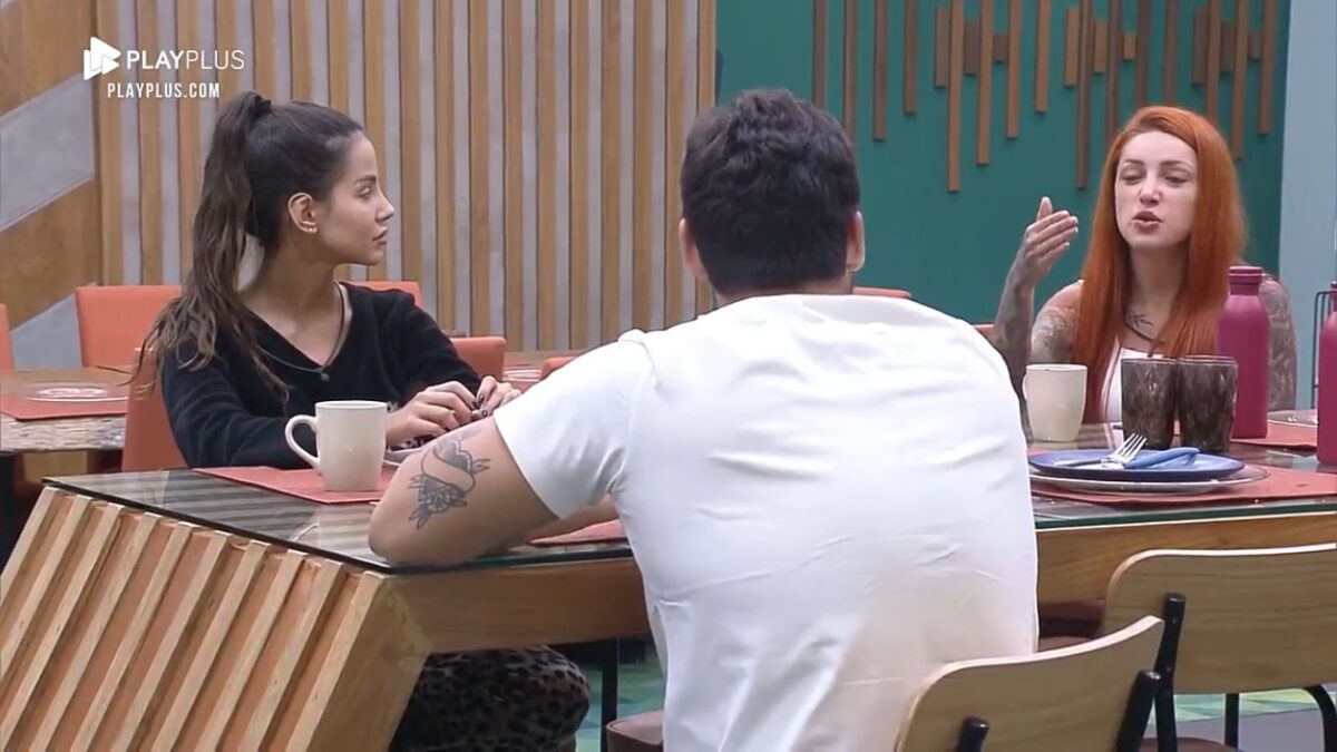 Na mesa do Power Couple, Luana de frente para Hadad e Brenda ao lado com as mãos levantadas.