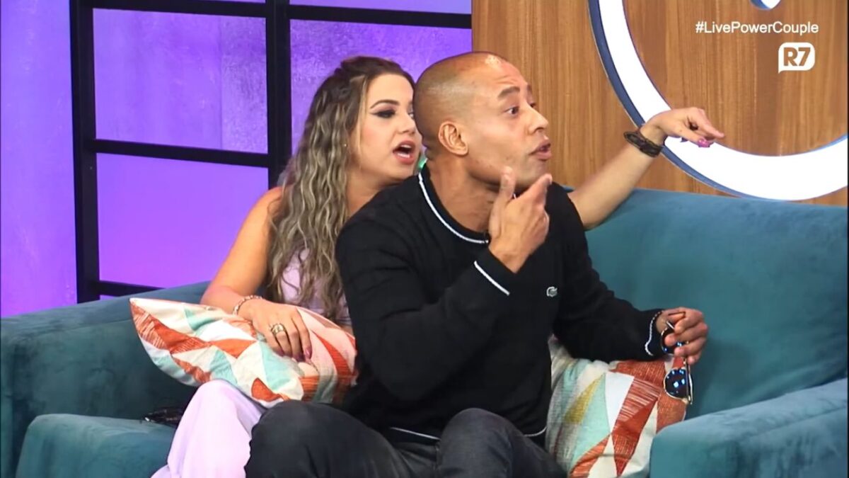 Karol e Mussunzinho sentados no sofá no cenário da live no Power Couple.