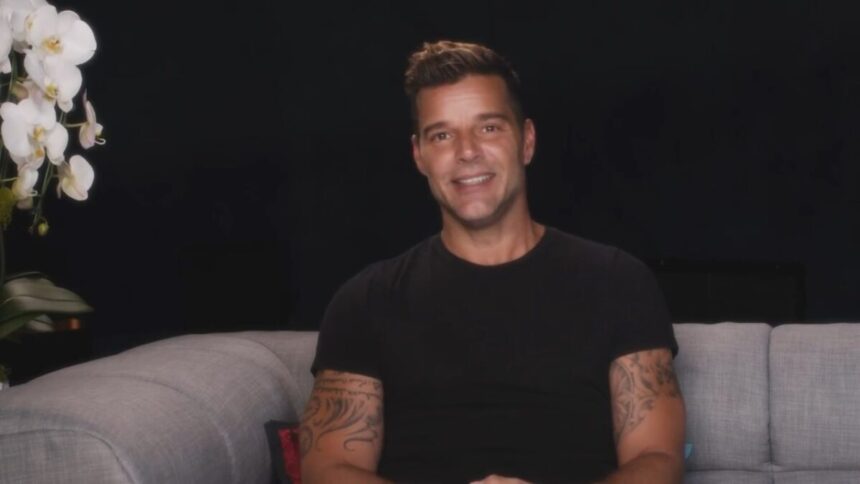 Ricky Martin sentado em um sofá vestindo preto