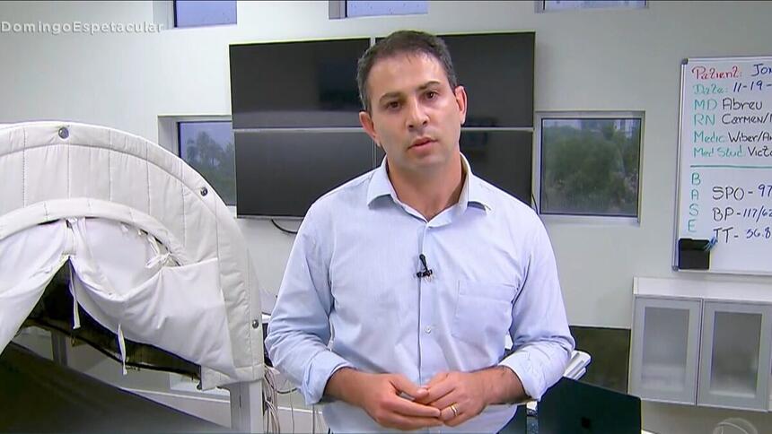 André Tal com camisa social azul clara dentro de um consultório nos Estados Unidos gravando matéria para o Domingo Espetacular, da Record TV