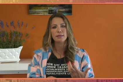 Bárbara Coelho participando do Encontro, via videoconferência pelo telão. Ela gesticula com as mãos