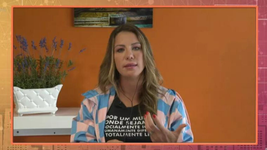 Bárbara Coelho participando do Encontro, via videoconferência pelo telão. Ela gesticula com as mãos