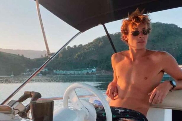 Bruno Krupp sem camisa e de óculos esculos, pilototando um pequeno barco em uma praia