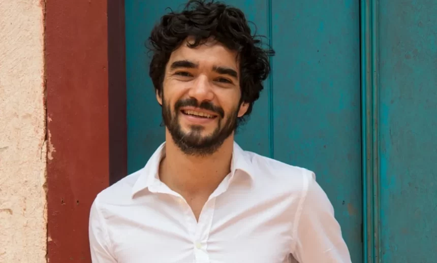 Caio blat, de camisa social branca, sorrindo, durante ensaio fotográfico