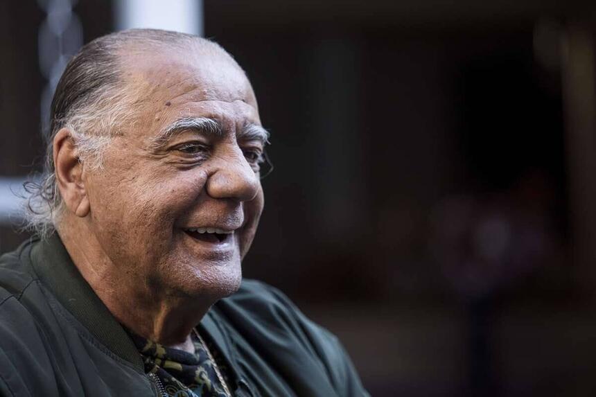 César Maluco de perfil, sorrindo, com a camisa do Palmeiras, próximo a uma van no backstage antes do jogo