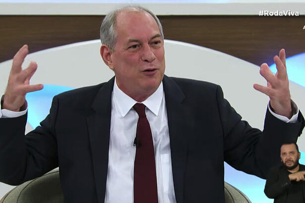 Ciro Gomes de palitó preto e gravata marrom, sentado, gesticulando durante entrevista no Roda Viva, da TV Cultura