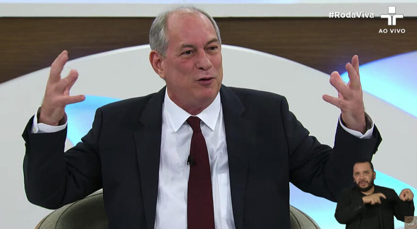 Ciro Gomes de palitó preto e gravata marrom, sentado, gesticulando durante entrevista no Roda Viva, da TV Cultura