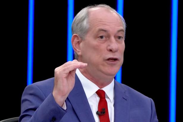 Ciro Gomes de blazer azul, camisa branca e gravata vermelha com semblante sério, sentado durante entrevista no jornal nacional, da TV Globo