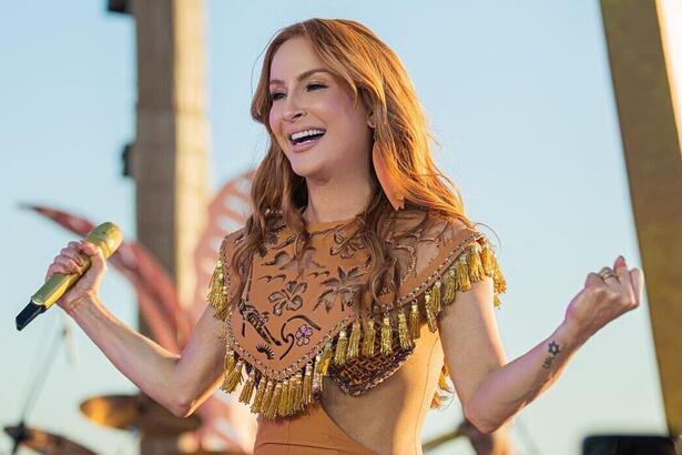 Claudia Leitte com os braços abertos, sorrindo, durante gravação do dvd Prainha da Claudinha