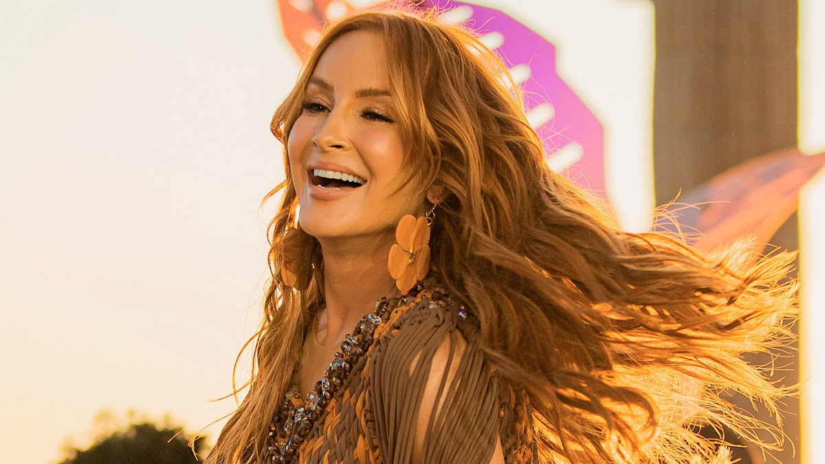 Claudia Leitte sorrindo, de top marrom e laranja, cabelo solto e brancos florais durante gravação de dvd