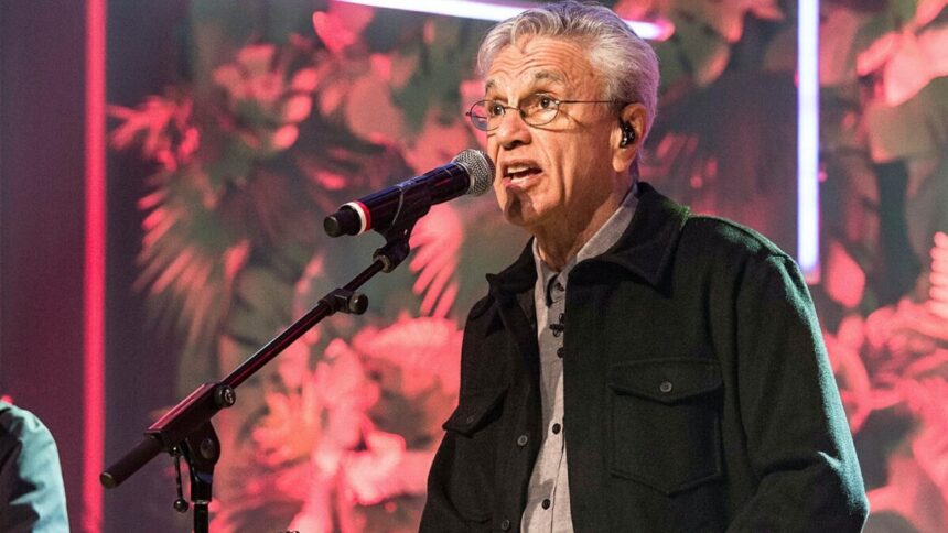 Caetano Veloso com camisa manga longa preta, sentado num banco com o microfone próximo a boca durante gravação do Conversa com Bial da TV Globo