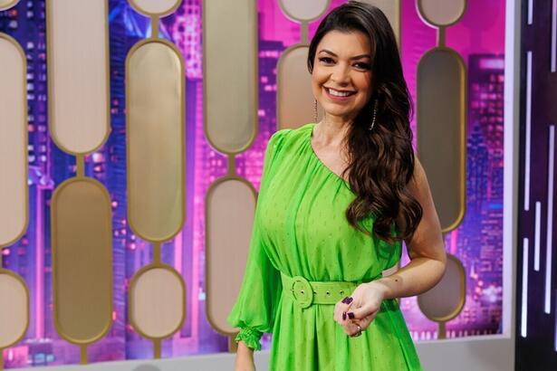 Amanda Françozo sorrindo, com vestido verde (tomara que caia), cabelo para o lado esquerdo durante gravação do De Papo com Amanda Françozo da TV Aparecida