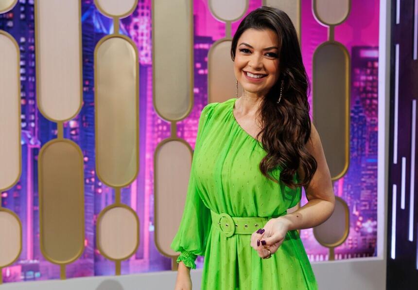 Amanda Françozo sorrindo, com vestido verde (tomara que caia), cabelo para o lado esquerdo durante gravação do De Papo com Amanda Françozo da TV Aparecida