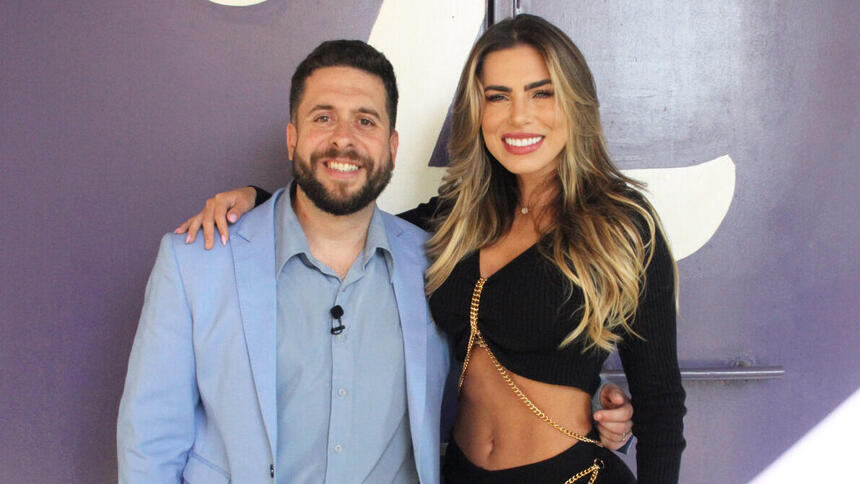 Erika Schineider de top e calça preta, cabelo solto, sorrindo, com a mão no ombro de Mauricio Meirelles; mauricio meirelles de blazer e camisa social azul, sorrindo, de barba, durante os bastidores da gravação do Foi Mau, da RedeTV! | Imagem: Reprodução/RedeTV!