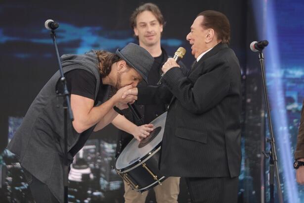 Tato, de chapéu e camisa preta, beijando a mão de raul gil durante o quadro de homenagens