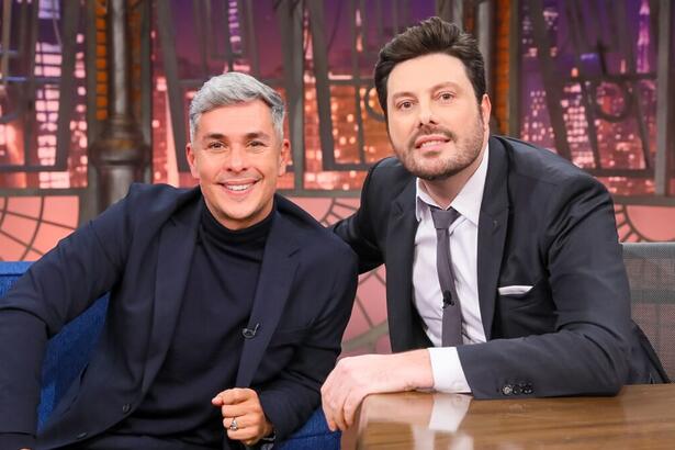 Ivan Moré de blazer e camisa preta, com o braço encostado no sofá azul, ao lado de Danilo Gentili durante gravação do The Noite, do SBT